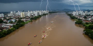 Crise Climática: Novas Medidas de Prevenção e Alerta em 15 Estados a Partir de 2025 Vista aérea de uma cidade brasileira afetada por uma enchente severa, com equipes de resgate em ação e infraestrutura danificada, simbolizando os impactos da crise climática.